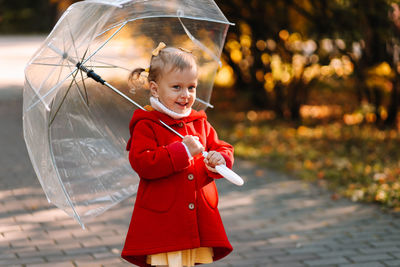 Cute girl holding umbrella while standing outdoors