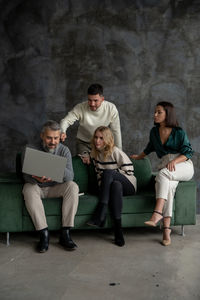 Friends using digital tablet while sitting against wall