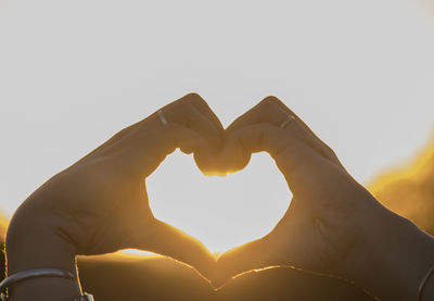 Close-up of human hands making heart shape against clear sky during sunset