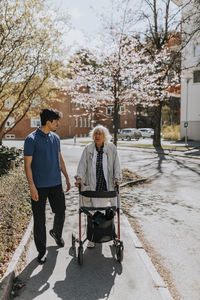 Male caregiver walking with senior woman using walker on sidewalk