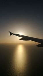 Silhouette airplane flying in sky during sunset