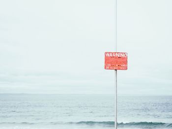 Warning sign on pole in sea against sky