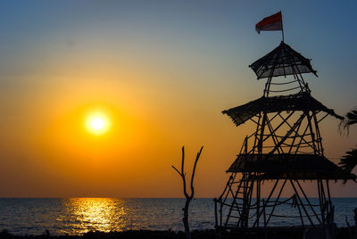 Silhouette tower by sea against sky during sunset