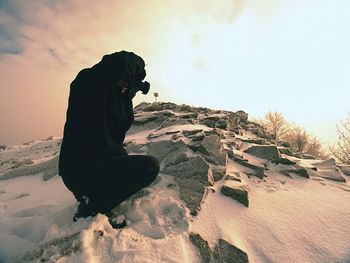 Photographer lay in snow on mountain peak and takes a picture of  landscape around, snowy winter day