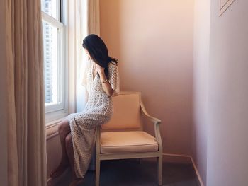 Side view of woman sitting on chair at home