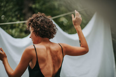 Rear view of woman with arms raised standing outdoors