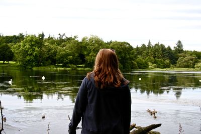 Rear view of woman standing on field by lake against sky