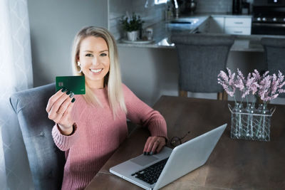 Smiling young woman using mobile phone at table