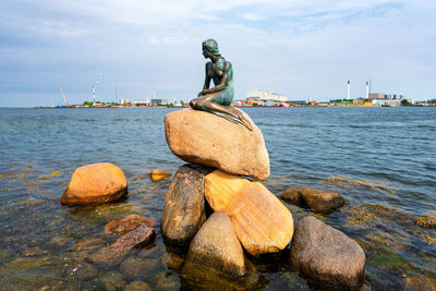 Statue on rock by sea against sky