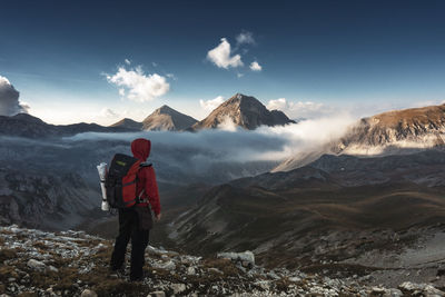 Rear view of man standing on mountain against sky