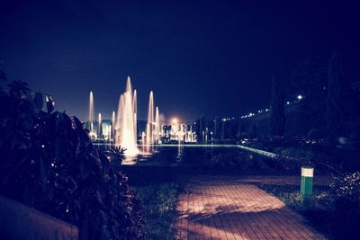 Illuminated fountains in garden against sky at night