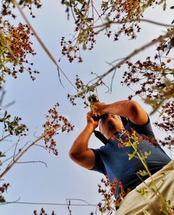 Low angle view of man holding flowering tree against sky