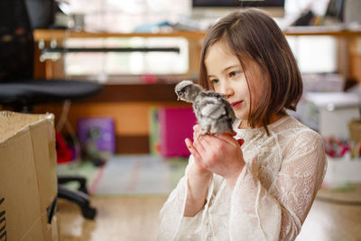 A little girl holds a tiny baby chick close to her face to observe