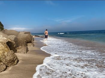 Man on rocks at beach against sky