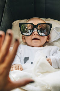 From above of newborn infant in pajama with open mouth in sun glasses lying on bed at home