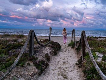 Rear view of woman walking on beach against sky
