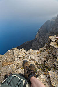 Low section of person on rock against sky