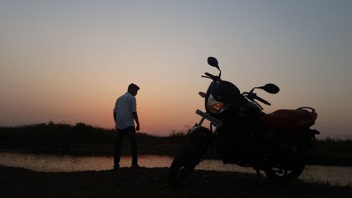 Rear view of man with motorcycle against sky during sunset