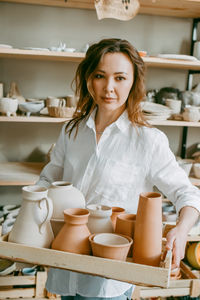 Woman master of pottery workshop carries clay products for firing