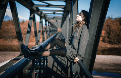 Woman with bicycle on railing against bridge