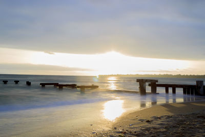 Broken pier in sea against cloudy sky at morning