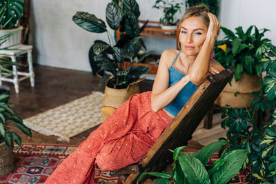 Portrait of a young beautiful thoughtful woman sitting on a wooden chair among plants.