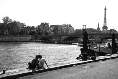 Rear view of people sitting on bridge over river