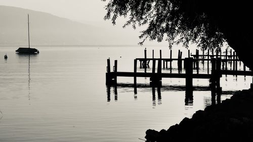 Silhouette wooden posts in sea against sky