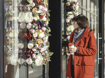 Woman in red duffle coat walks pass florist shop. woman goes along sunny side of street