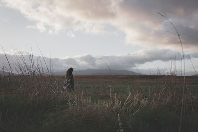 Rear view of woman walking on field against sky