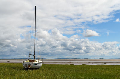 Sailboat moored on grassy field against cloudy sky