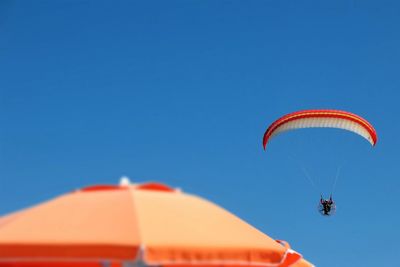 Low angle view of person paragliding against clear blue sky on sunny day