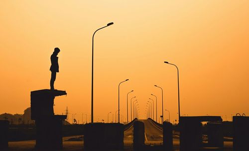 Silhouette young man standing on built structure against clear sky during sunset