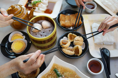 Cropped image of people having food with chopsticks at table