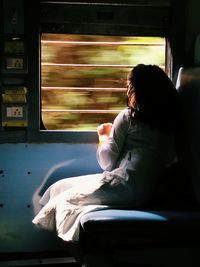 Rear view of woman sitting on bed at home