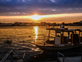 Sailboats moored on sea against sky during sunset
