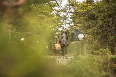 Couple carrying blanket and basket in forest seen through plants