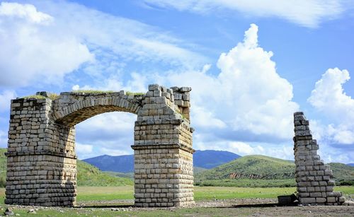 Old ruins on field against cloudy sky