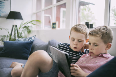 Brothers using digital tablet on sofa at home