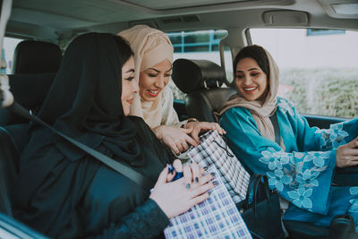 Cheerful women wearing hijab sitting in car with shopping bags