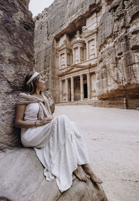 Woman sitting on rock against historic building