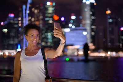 Portrait of smiling woman standing in illuminated city at night