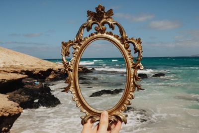 Cropped hand of woman holding picture frame at beach against sky