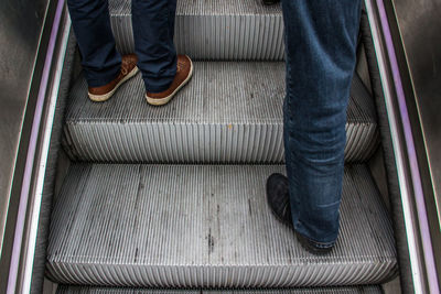 Low section of men standing on escalator