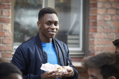 Portrait of smiling teenage boy holding food while standing outdoors