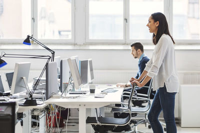 Side view of young businesswoman with colleague working in background at office