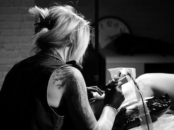 Rear view of tattooist making tattoo on customer