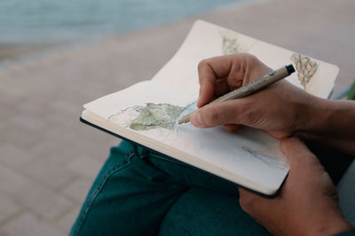 Midsection of man sketching in book on footpath