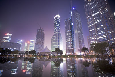 Illuminated modern buildings in city against sky at night