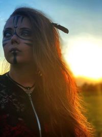 Close-up portrait of a beautiful young woman against sunset sky